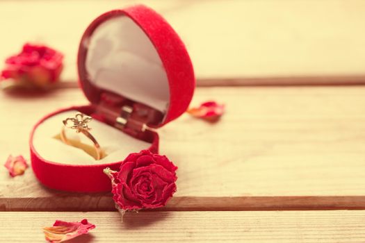 Golden engagement ring in a heart shaped box and roses