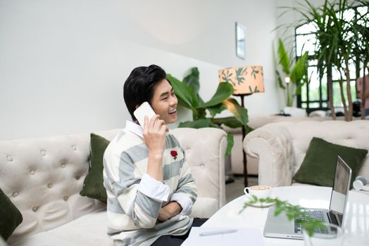 Asian businessman using mobile phone while working with laptop on table in coffee shop