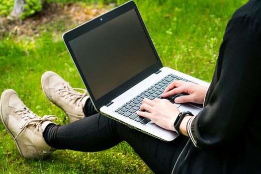 A woman is sitting on the grass while using laptop computer