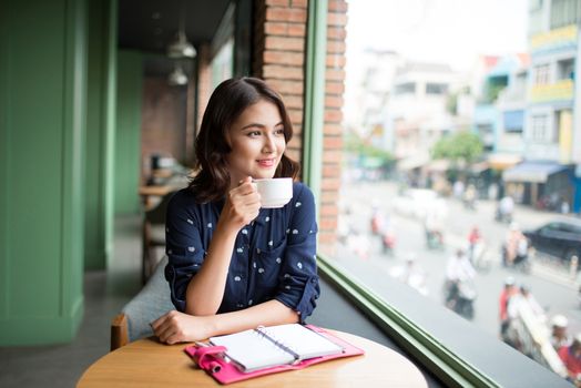 Portrait of happy young business woman with mug in hands drinking coffee in the morning at restaurant