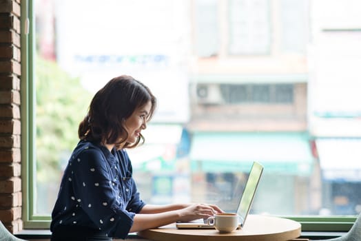 Beautiful cute asian young businesswoman in the cafe, using laptop and drinking coffee smiling