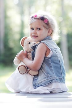 Pretty girl playing with teddy bear outdoors