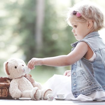 Pretty girl playing with teddy bear outdoors