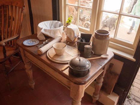 an array of old kitchen utensils and pots and plates and knives and forks on a nice wooden table near a window on a sunny day