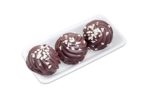 Three cookies with whipped egg whites, glazed with dark chocolate and sprinkled with chunks of white chocolate on the small plastic tray on a light background
