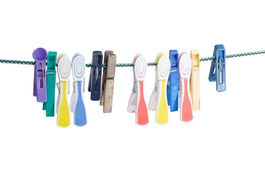 Several different spring-type new and old varicolored plastic clothespins and one old wooden clothespin hanging on the clothes line on a light background
