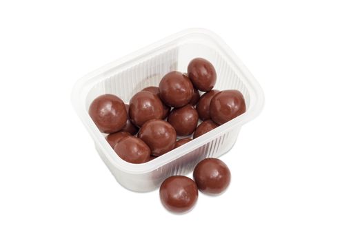 Malted milk balls covered milk chocolate in the small transparent plastic container and two candies separately beside on a light background
