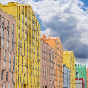 Fragment of a multicolored facade of the modern multi-story apartment complex against the background of the sky with clouds
