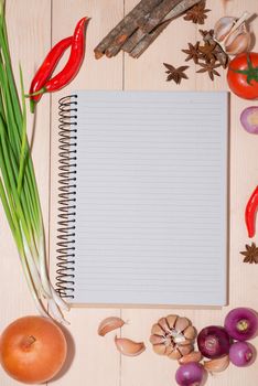 Open recipe book with fresh vegetables on wooden table.