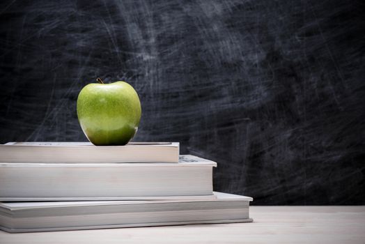 Apple on top of books with chalkboard.