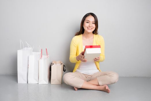 Young asian woman sitting besides row of shopping bags holding red gift box