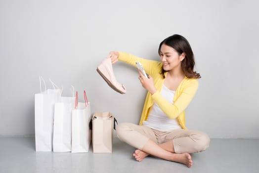 Young surprised asian woman sitting besides row of shopping bags, happy with new shoes
