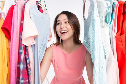 Young asian woman surprised in shop, peeking out through clothing in clothes rack 