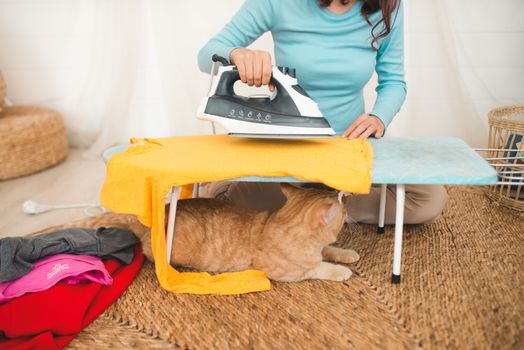 Happy young asian woman ironing clothes sitting on floor at home.