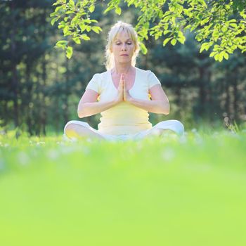 Beautiful mature woman in lotus yoga position in summer park
