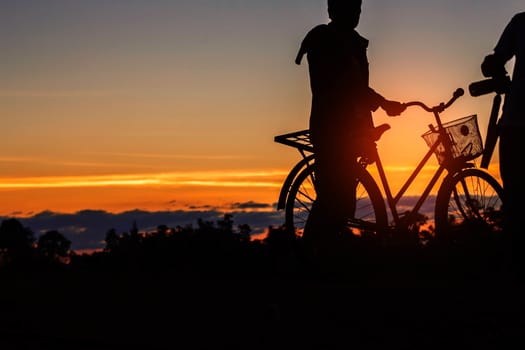 young man with a bicycle on a field at sunset.