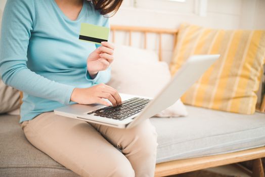 Online shopping concept. Young asian woman holding credit card and using laptop computer. 