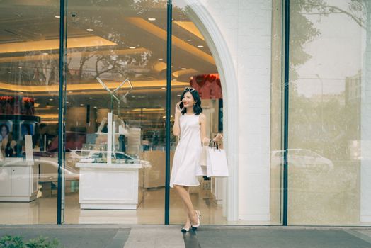 Beautiful asian girl with shopping bags listening to mobile phone standing outside the mall