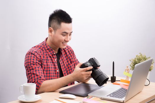 Professional photographer. Portrait of confident young man in shirt holding hand on camera while sitting at his desk.