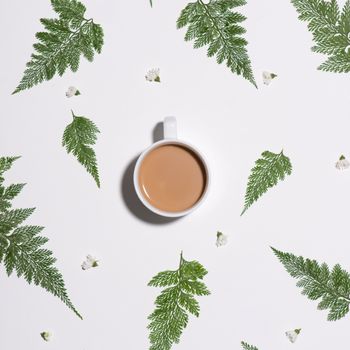 Flat lay of green leaves pattern with cup of  coffee on white background