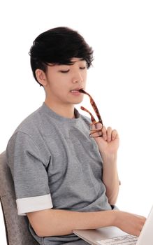 A young Asian man sitting and working hart on his laptop to solve the
problem, with glasses in his mouth, isolated for white background.
