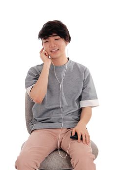 A handsome young Korean man sitting in a gray t-shirt and listening
to music whit his earphone from his phone, isolated over white. 
