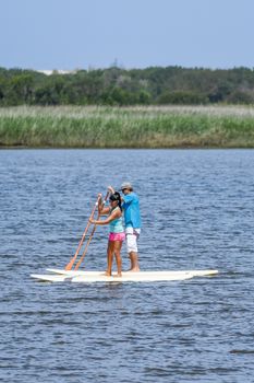 Man and woman stand up paddleboarding on lake. Young couple are doing watersport on lake. Male and female tourists are in swimwear during summer vacation.