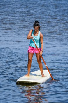 Woman stand up paddleboarding on lake. Young girl doing watersport on lake. Female tourist in swimwear during summer vacation.