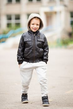 Full-length portrait of adorable little boy wearing black leather jacket. Urban kids. Hands in pockets. Loss of primary teeth in children.