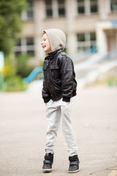 Full-length portrait of adorable little urban boy wearing black leather jacket. City style. Urban kids. Kid jumping and having fun outdoors