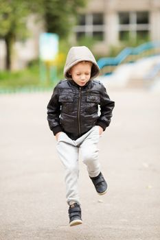 Full-length portrait of adorable little urban boy wearing black leather jacket. City style. Urban kids. Kid jumping and having fun outdoors