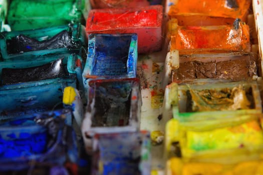 artists brushes and watercolour paints on palette. Vintage stylized photo of paintbrushes closeup and artist palette. Used palette with paintbrush. Old messy set of watercolor paints