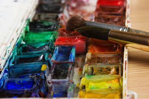 artists brushes and watercolour paints on palette. Vintage stylized photo of paintbrushes closeup and artist palette. Used palette with paintbrush