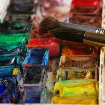 artists brushes and watercolour paints on palette. Vintage stylized photo of paintbrushes closeup and artist palette. Used palette with paintbrush