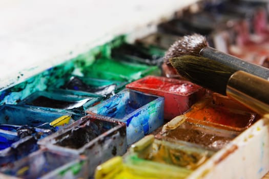 artists brushes and watercolour paints on palette. Vintage stylized photo of paintbrushes closeup and artist palette. Used palette with paintbrush