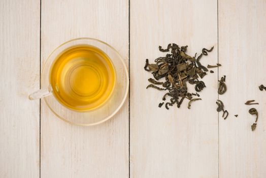 Black tea in a glass cup and tea leaves in wooden spoon on white wooden background.