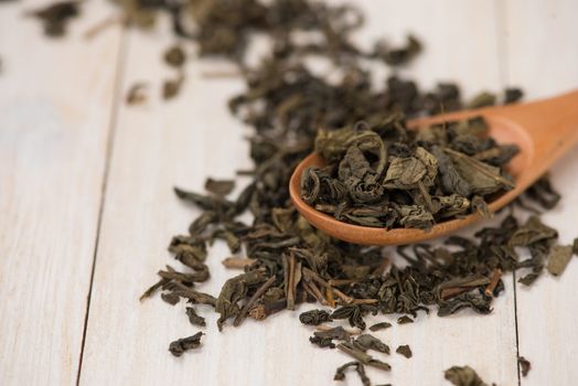 Black tea in a glass cup and tea leaves in wooden spoon on black stone background.