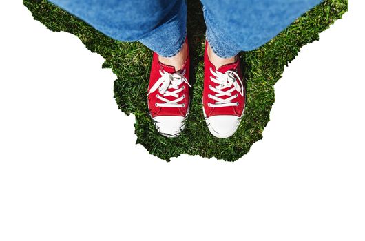 Legs in old red sneakers on green grass. View from above. The concept of youth, spring and freedom. Isolated on white background.