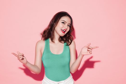 Young attractive asian woman with professional makeup singing and dancing on pink background.