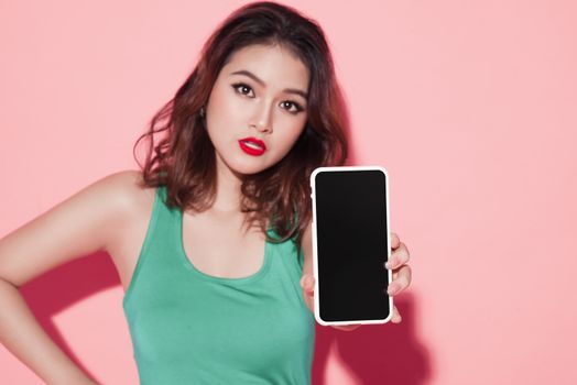 Asian girl showing smartphone screen on pink background.