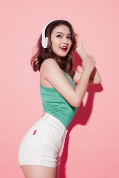Young attractive asian woman with professional makeup singing and dancing while listening to music on pink background.