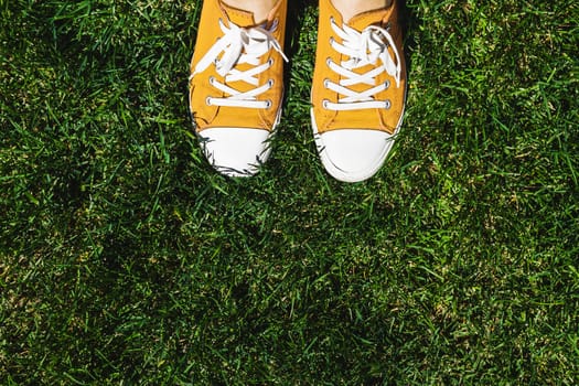 Legs in old yellow sneakers on green grass. View from above. The concept of youth, spring and freedom.