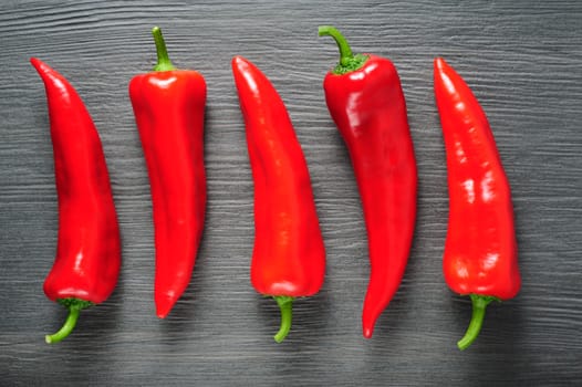 Five ripe sweet red Kapia peppers on dark shale stone background