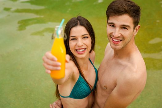 Young couple inside the pool and drinking natural juices