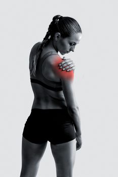 Studio shot of a sporty young woman holding her shoulder in pain