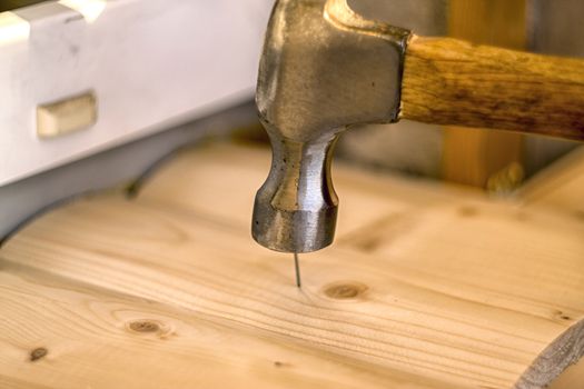 Hammer clogs a nail into a wooden board.