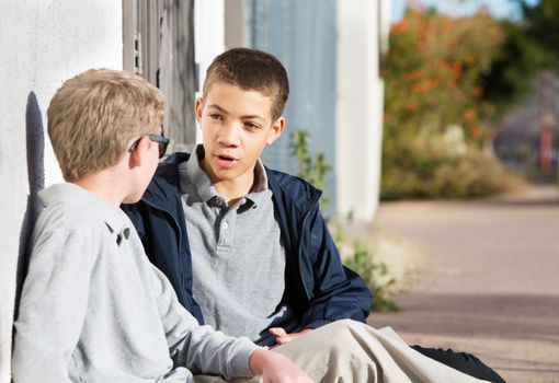 Teen male talking to friend seated outside on ground