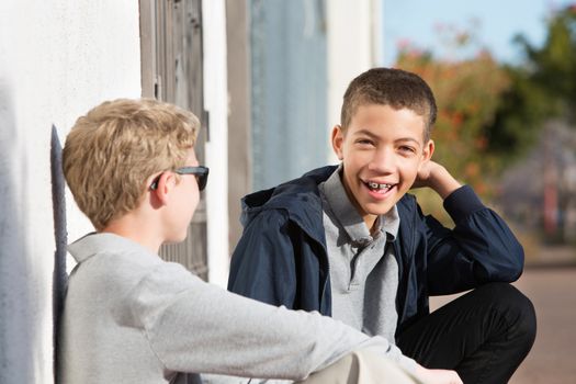 Laughing African American teen with braces sitting outside with blond friend