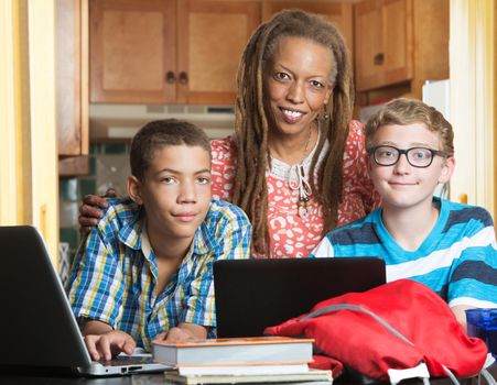 Smiling mother with son and his friend doing homework in kitchen
