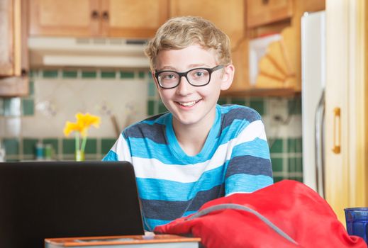 Cute single smiling boy in eyeglasses and striped shirt using laptop